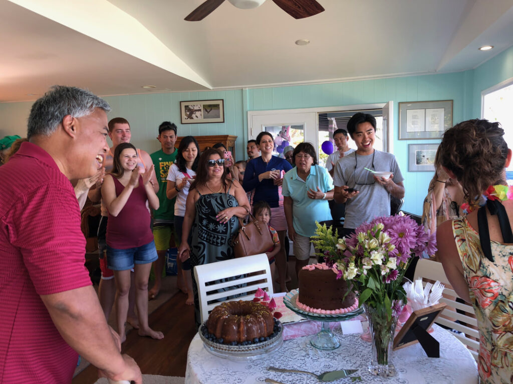 Family and friends gather around a birthday cake in a cozy living room.