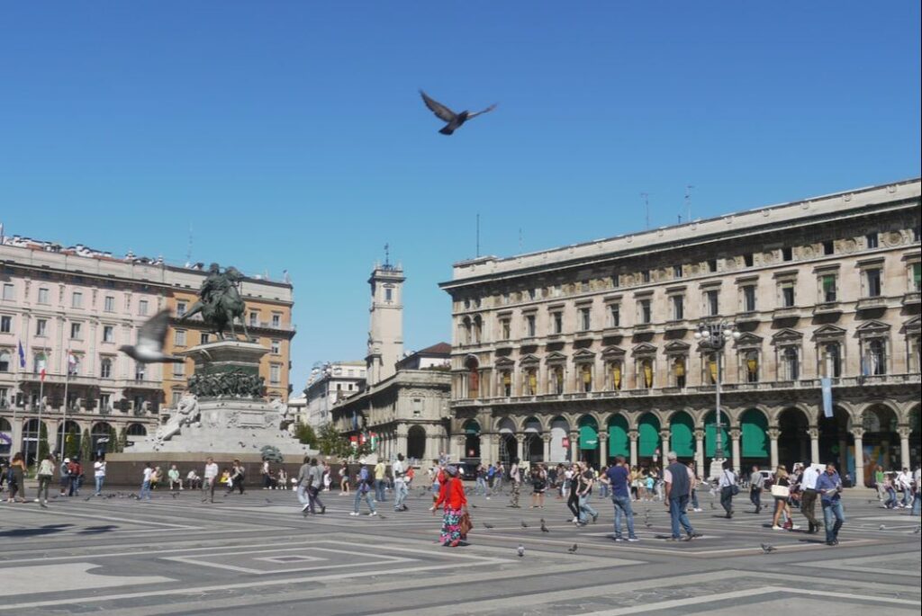 A bird flies over a bustling city square with historic buildings.