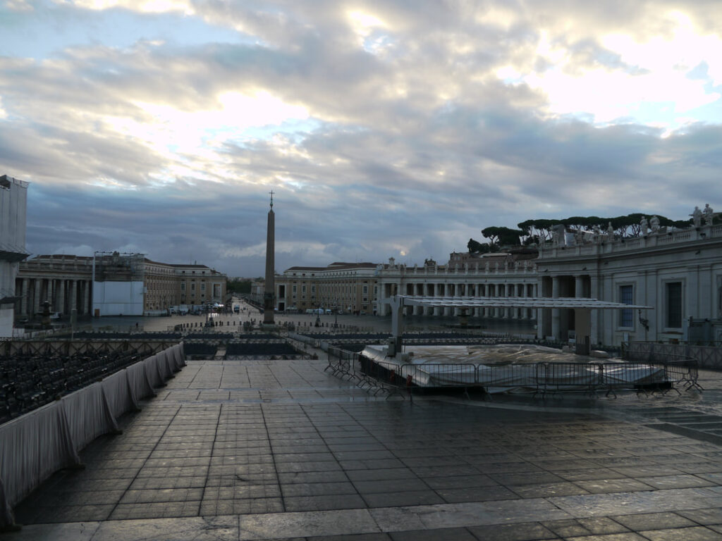View of a city square with an obelisk and cloudy sky at dusk.