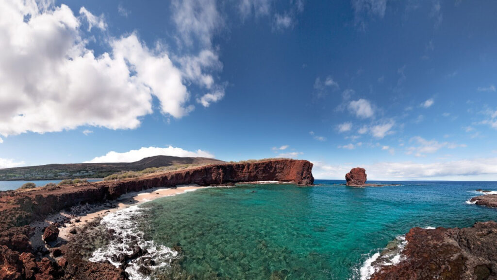 Scenic coastal cliffs overlooking clear turquoise waters under a partly cloudy sky.