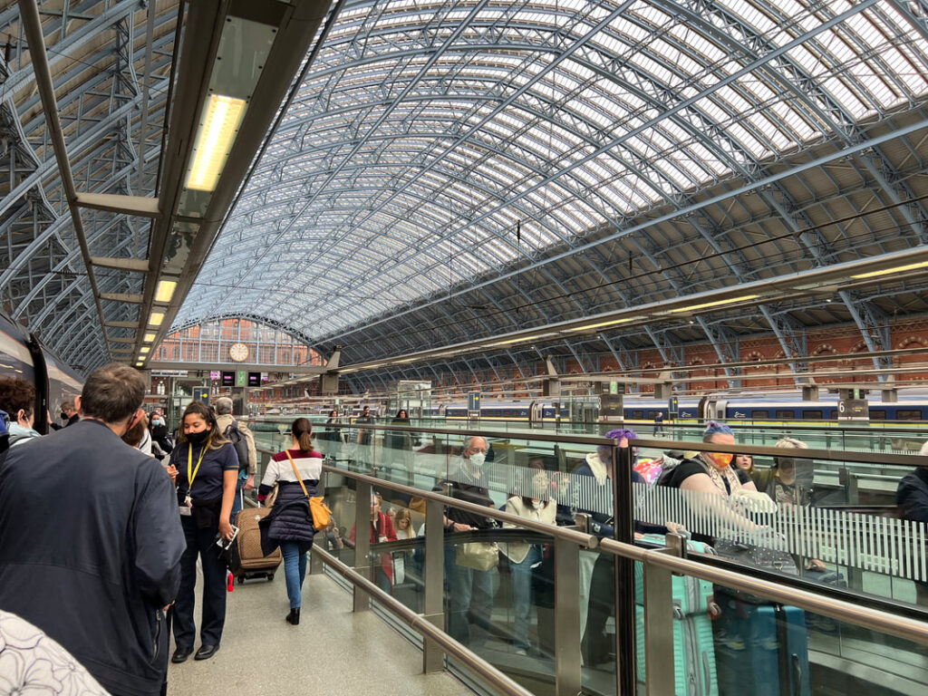 Busy train station with a large arched glass roof and passengers walking.